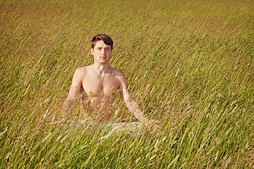 Image showing Man sits in grass in lotus pose