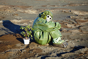 Image showing Man in chemical suit and houseplant in desert