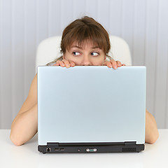 Image showing Young woman hiding behind a laptop