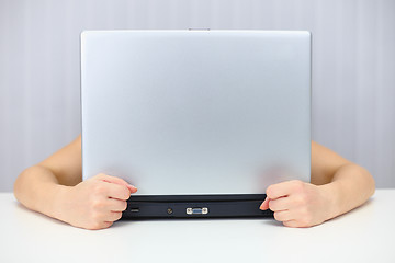 Image showing Emotional woman hiding behind a laptop