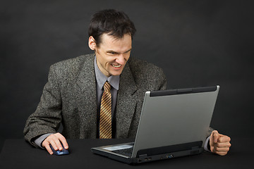 Image showing Furious man sits at table and looks at laptop screen