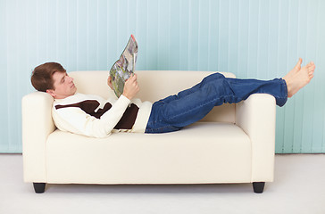 Image showing Young woman lies comfortably on sofa with a magazine