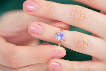 Image showing Golden ring with blue jewel try on a finger