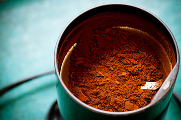 Image showing Electrical coffee-mill machine with milled ground coffee on the green tabletop with top cover removed