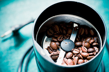 Image showing Electrical coffee-mill machine with roasted coffee beans on the green tabletop with top cover removed