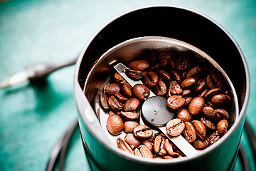 Image showing Electrical coffee-mill machine with roasted coffee beans on the green tabletop with top cover removed