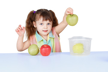 Image showing Little girl playing with green apples sitting at table