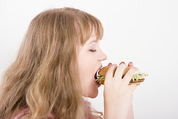 Image showing The girl bites a hamburger