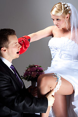 Image showing Young bride hitting groom while he takes off wedding garter