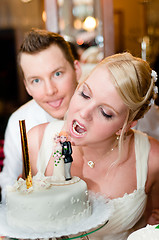 Image showing Young bride is going to bite her cake with groom in background