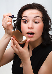 Image showing Woman is applying mascara while looking in mirror