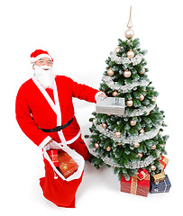 Image showing Santa Claus offering present in front of Christmas tree