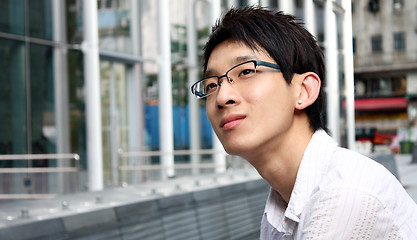 Image showing businessman sitting on a bench in front of an office building 