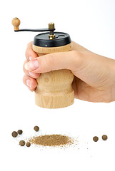 Image showing Wooden spice handmill in hand and allspice 