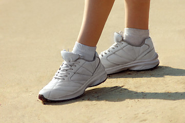 Image showing Female legs in sneakers on sand