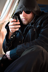 Image showing Hooded man looking at his cellular phone in an old airplane