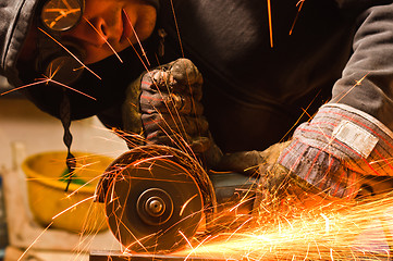 Image showing Worker cutting metal with many sharp sparks