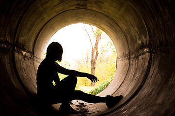 Image showing Silhouette of a young girl smoking in sewer pipe