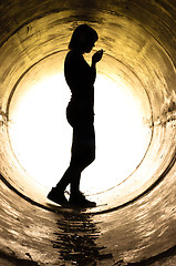 Image showing Silhouette of a young girl smoking in sewer pipe