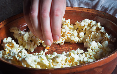 Image showing Hand taking out popcorn from brown dish