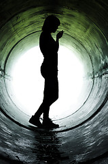 Image showing Silhouette of a young girl smoking in sewer pipe