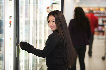 Image showing Young woman smiling while opening refrigerator in supermarket