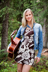 Image showing Female holding guitar against trees