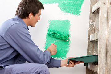 Image showing Mature man painting the wall with a roller