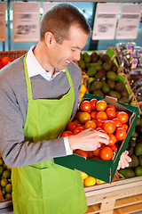 Image showing Happy market assistant holding box of tomatoes