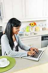 Image showing Young woman using computer in kitchen