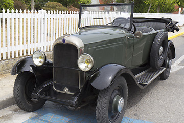 Image showing Green convertible classic car parked near a white fence.