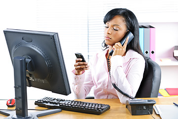 Image showing Black businesswoman using two phones at desk