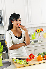 Image showing Young woman tasting vegetables in kitchen