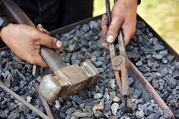 Image showing Detail of dirty hands holding hammer and pliers - blacksmith