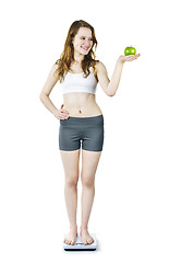 Image showing Young smiling girl on bathroom scale holding apple