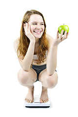 Image showing Young smiling girl on bathroom scale holding apple