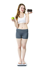 Image showing Young girl on scale holding apple and cake