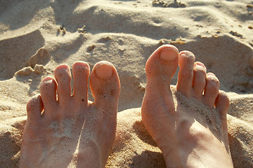 Image showing Human legs lying on coastal hot sand