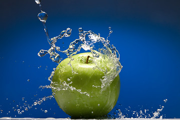 Image showing Green apple with water splash on blue background