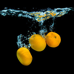 Image showing Fresh tangerines dropped into water with bubbles on black