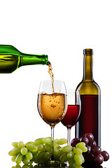 Image showing White wine pouring into glass with grape and bottles isolated