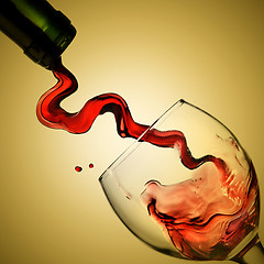 Image showing Pouring red wine in goblet on yellow background