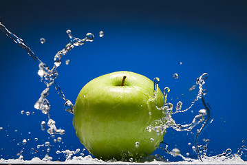 Image showing Green apple with water splash on blue background