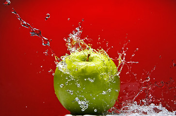 Image showing Green apple with water splash on red background