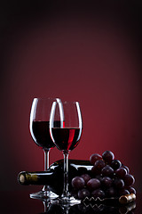 Image showing Wine in glasses with grape and bottle on red