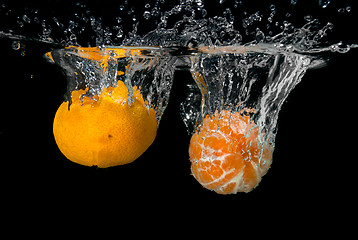 Image showing Fresh tangerines dropped into water with bubbles on black