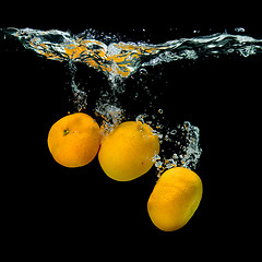 Image showing Fresh tangerines dropped into water with bubbles on black