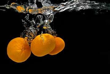 Image showing Fresh tangerines dropped into water with bubbles on black