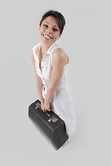 Image showing Smiling brunette with travel bag in white dress