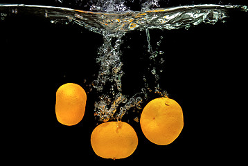 Image showing Fresh tangerines dropped into water with bubbles on black